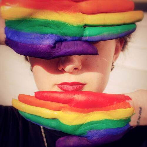 Woman* with rainbow painted hands in front of her face