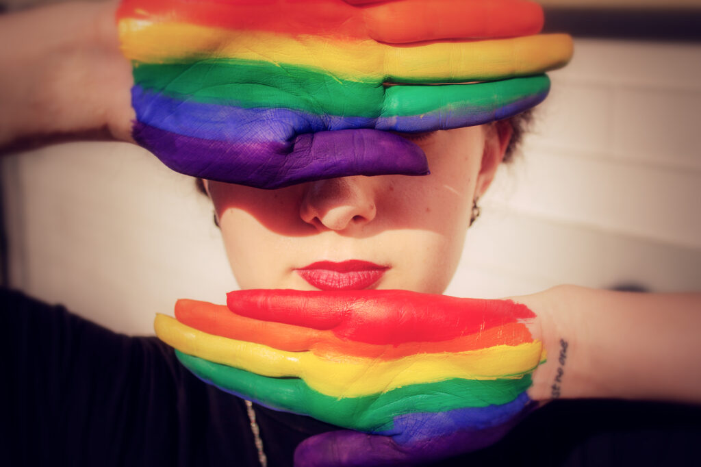 Woman* with rainbow painted hands in front of her face